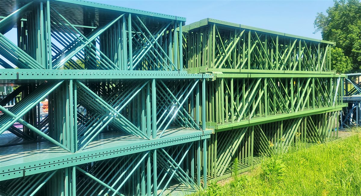 Green used pallet rack uprights stacked and stored upright on the lot